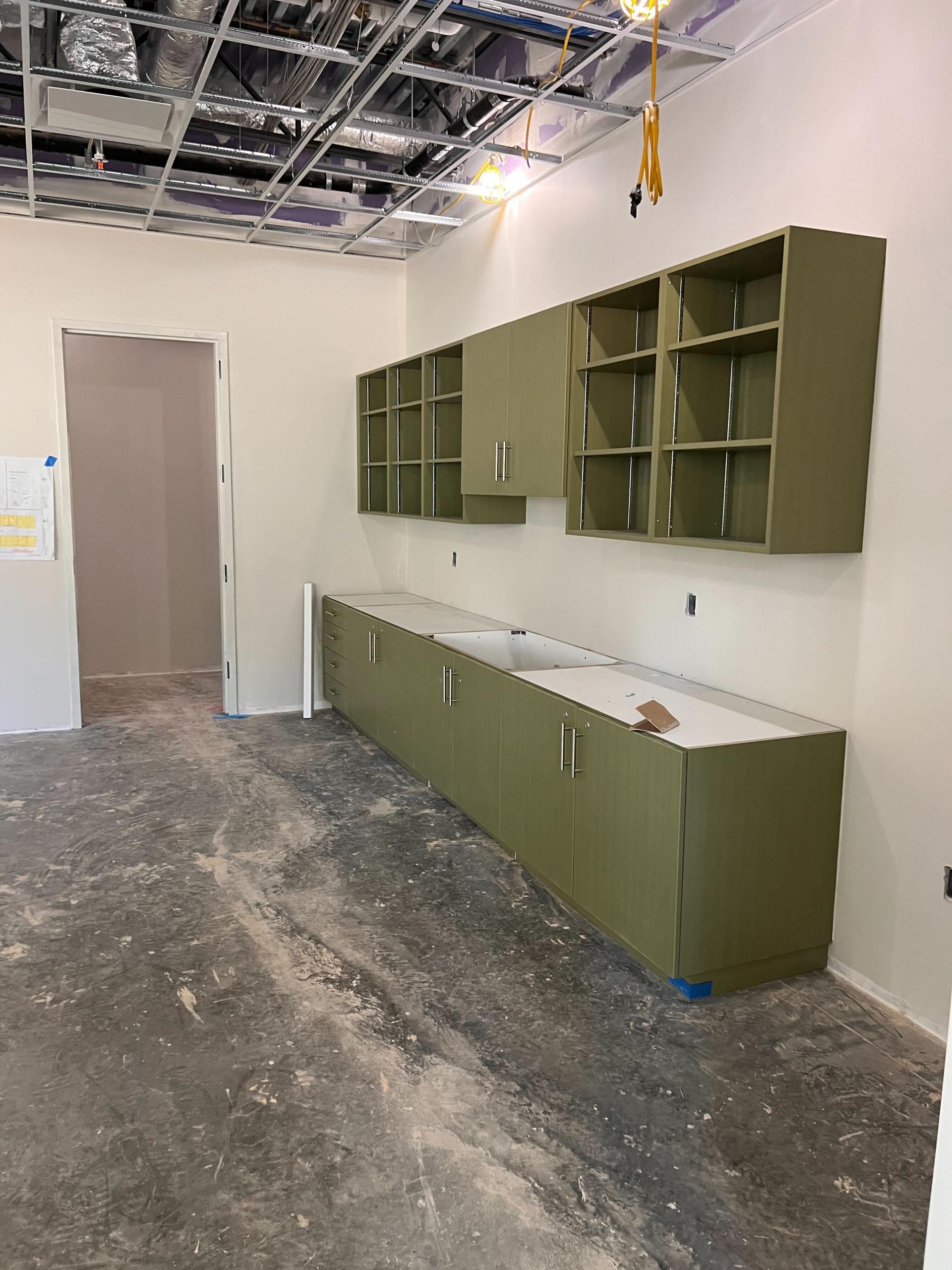 Photo of the SWRL under construction showing a set up of upper and lower cabinets in a room with unfinished concrete floors and walls.